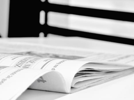 The daily newspaper on the table. Photo is black and white. Blind in the background.