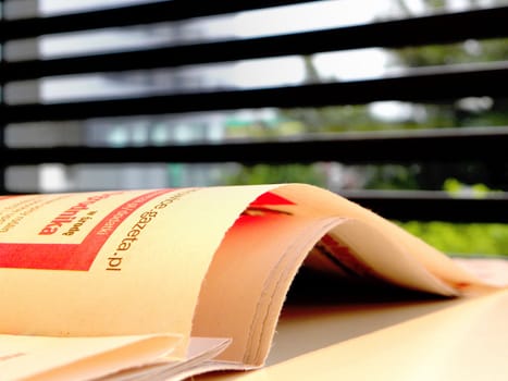 The daily newspaper on the table. Window and blind in the background. 