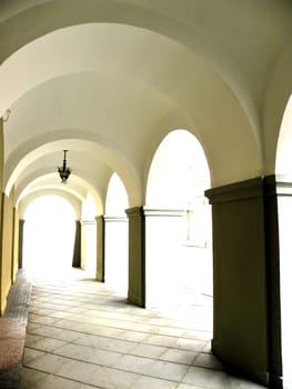 Bright arch with dark columns and one lamp. Silhouette of buildings in the background.