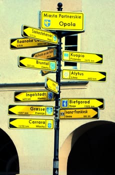 The yellow signposts with names of city. Building in the background.