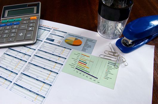 Budget speadsheet on a wooden desk with a calculator, stapler, and paper clips