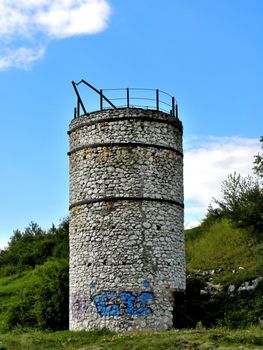 Single tower of stones with barrier. Sky with clouds and tree in the background. 