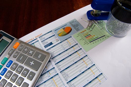 Budget on a wooden desk with a calculator, stapler, and paper clips