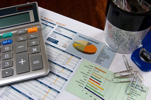 Budget on a wooden desk with a stapler, calculator, and paper clips