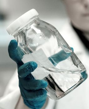 Chemist wearing blue latex gloves holding a flask full of liquid polymers in a research lab