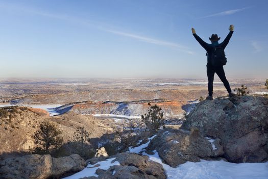 silhouette of happy male hiker standing on a rock and looking down to Horsetooth Reservoir, town of Fort Collins and Colorado plains, typical hazy winter scenery