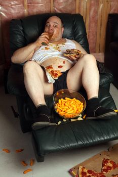 Lazy overweight male sitting on a couch watching television.  Harsh lighting from television with slow shutter speed to create TV watching atmosphere. Selective focus on the eyes.