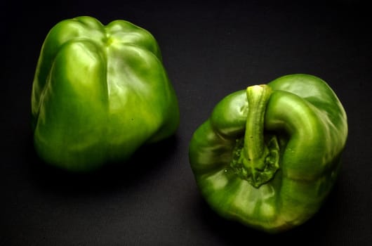 Two green sweet peppers isolated on black