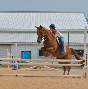 Athletic teen girl jumping a horse over rails.  Shot from the side as the horse's back legs are still on the ground.