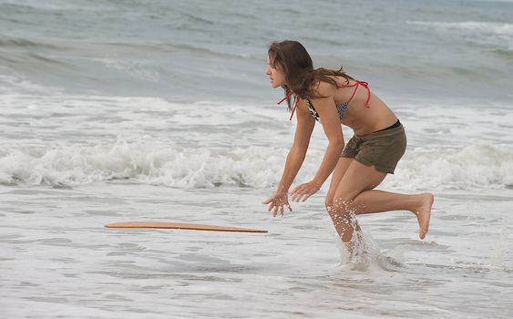 Athletic teen girl throwing skim board into surf at the beach in Emerald Isle, North Carolina.