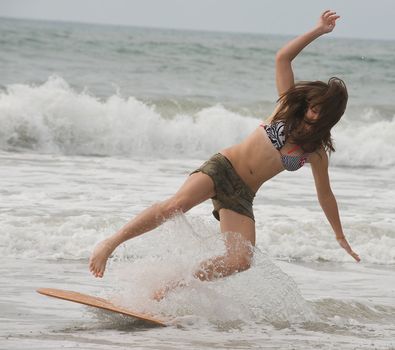 Athletic teen girl falling off a skim board into the surf in Emerald Isle, North Carolina.