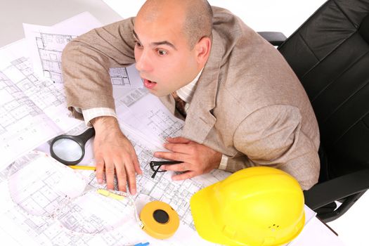 A businessman sleepy with architectural plans at desk