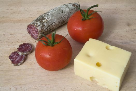 Sausage, tomatoes and cheese on a wooden chopping board.