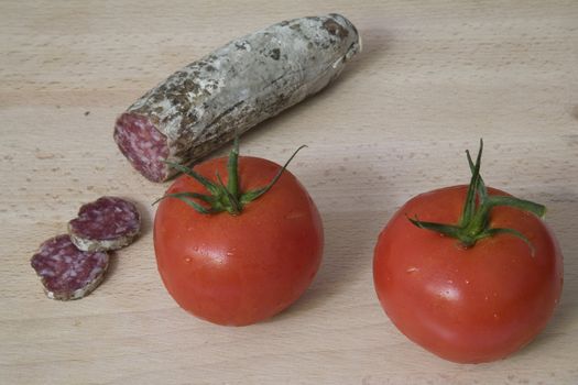 Mediterranean nibbles: sausage and tomatoes on a wooden chopping board.