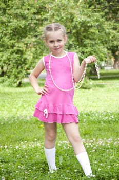 Full length portrait of a young blond girl in colurful dress, poses in the park, with beads around the neck