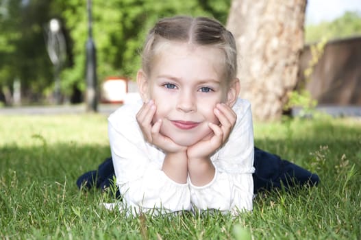 Young girl is lying on green grass and smile, in summer park