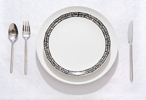 Empty pure plate on a table with an empty glass for wine, a spoon, a fork and a knife
