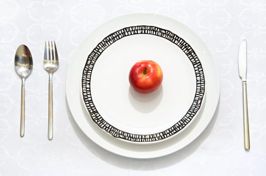 Red apple on a flat plate with a knife, a fork and a spoon
