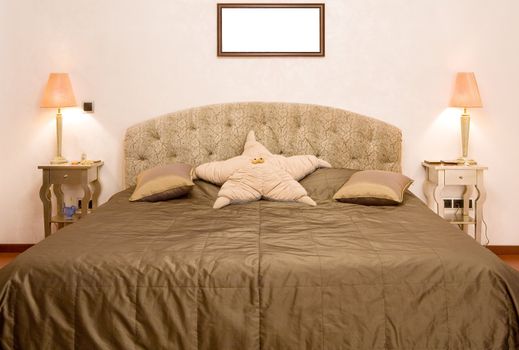 Bedroom in which there is a big bed with a coverlet of olive colour, two little tables with lamps and a pillow in the form of a star
