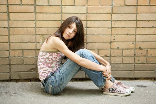 The girl sits before a brick wall
