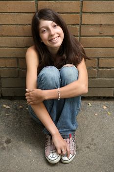 The  smiling girl sits before a brick wall
