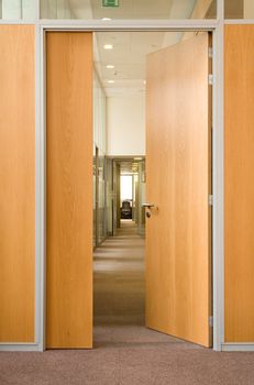 The open door in a long corridor in which other open doors in office centre are visible
