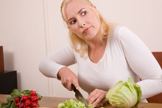 Pretty blond housewife looking very annoyed while cutting the vegetables