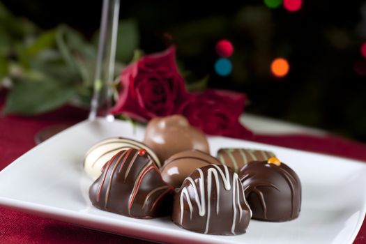 Gourmet chocolates on white plate with roses and sparkling lights.