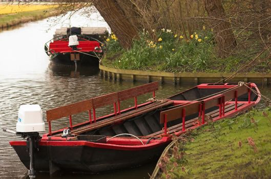 Motor boats moored at the edge of a canal next to a dutch field