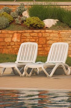 White plastic seats standing on a terrace next to a pool