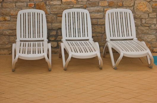 White plastic seats standing on a terrace next to a pool