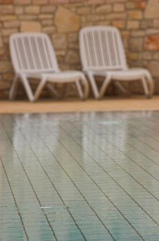 White plastic seats standing on a terrace next to a pool