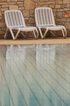 White plastic seats standing on a terrace next to a pool