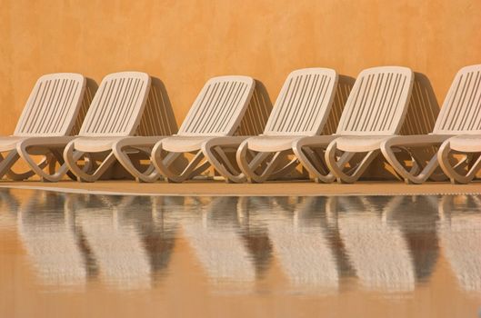 White plastic seats standing on a terrace next to a pool