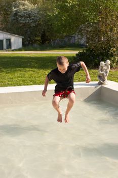 A young male boy splashes in a pool in his boxers and shirt on a warm spring day