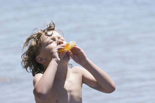 Face to the sun, a boy enjoys a cool ice block after a summer swim.