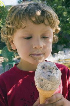 A boy eats an ice cream while shading under a tree