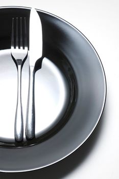 steel fork and knife on a black ceramic saucer isolated on white