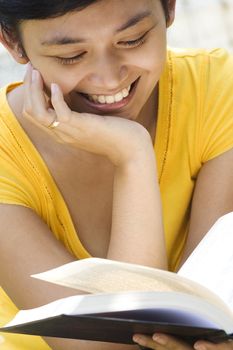 asian young woman smiling while reading a book outdoor