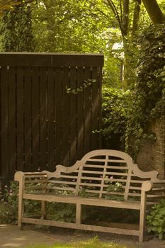 Wooden garden bench in shadow of a park wall