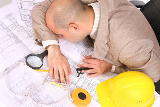 A businessman sleepy with architectural plans at desk