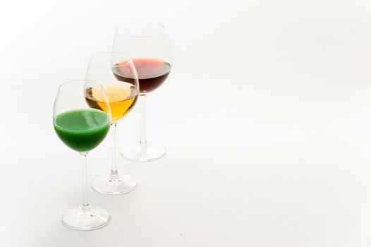 Three tall glasses on white background filled with: white, red wine and green cocktail