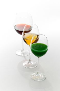 Three tall glasses on white background filled with: white, red wine and green cocktail