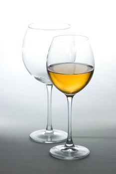 Two tall wine glasses on light background, one filled with white wine