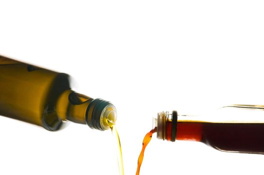 Olive oil and vinegar being poured from bottles isolated on white