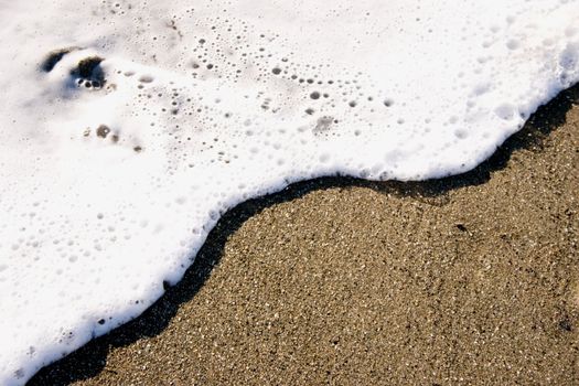 A small wave rolls up the sand like icing spreading on a sponge