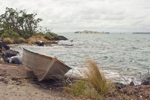 A dinghy rests on the shore of Rangitoto Island in the Hauraki Gulf of New Zealand. Browns Island is in the distance
