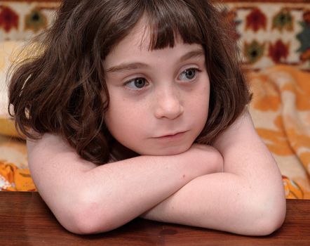 Serious cute little girl rests her head on crossed arms close-up