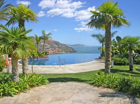 An infinity pool, surrounded with tropical foliage and with mountains and sea in the background