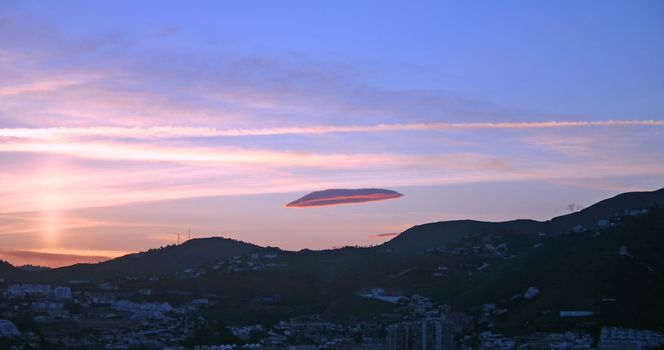 A single lenticular cloud, hovering above mountain and town at sunset